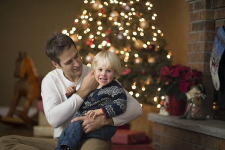 A father is holding his son by the Christmas tree.